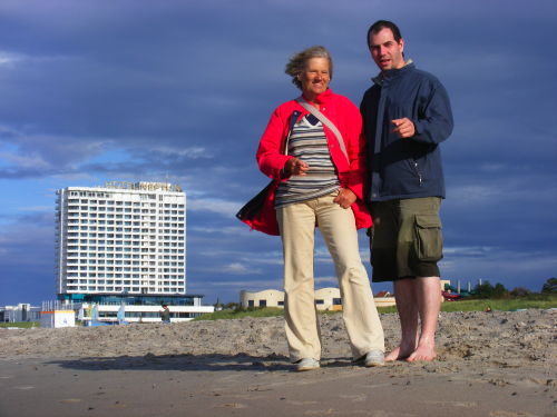 links das Hotel Neptun, rechts eine Frau und ein Mann am Strand